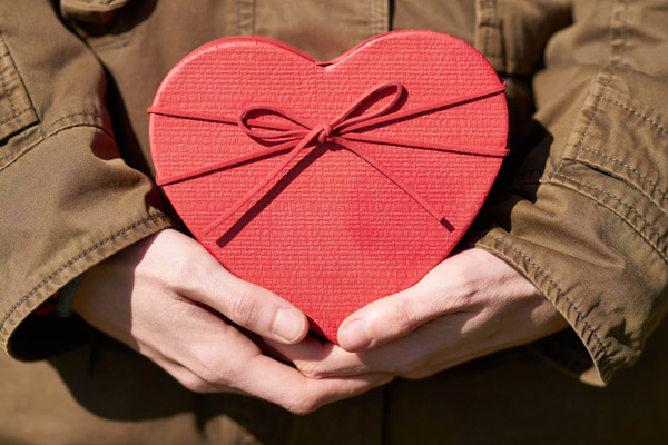 Foto: Mãos de homem segurando uma caixa de presentes vermelha, em formato de coração.