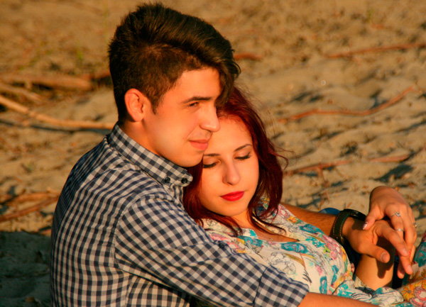 Foto: Casal de namorados abraçado, sentado na areia da praia.